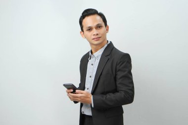 Mutlu Asyalı takım elbiseli iş adamı izole edilmiş arka planda akıllı telefon tutuyor.