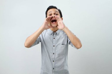 Genç Asyalı Endonezyalı bağırıyor ve izole edilmiş arka planda elleri ağızlarına dolanıyor.