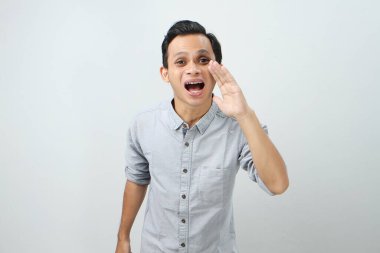 Genç Asyalı Endonezyalı bağırıyor ve izole edilmiş arka planda elleri ağızlarına dolanıyor.