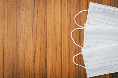 Kahverengi tahta kaplama arka planda tek kullanımlık cerrahi maskenin üstünde. Korunaklı beyaz yüz maskesi salgını Coronavirus karantinası, COVID-19 eski ahşap masa üzerinde fotokopi alanı.