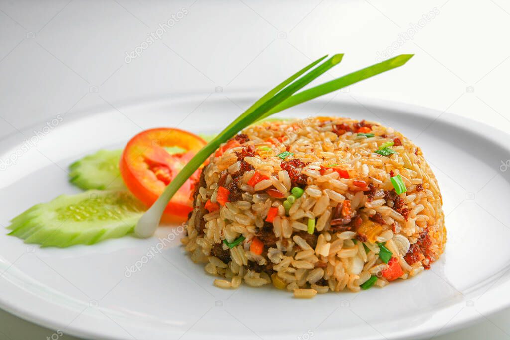 Asian fried rice with egg and vegetable in white ceramic plate on the table in the restaurant. Khao Pad popular traditional Thai style food. Front view with copy space.