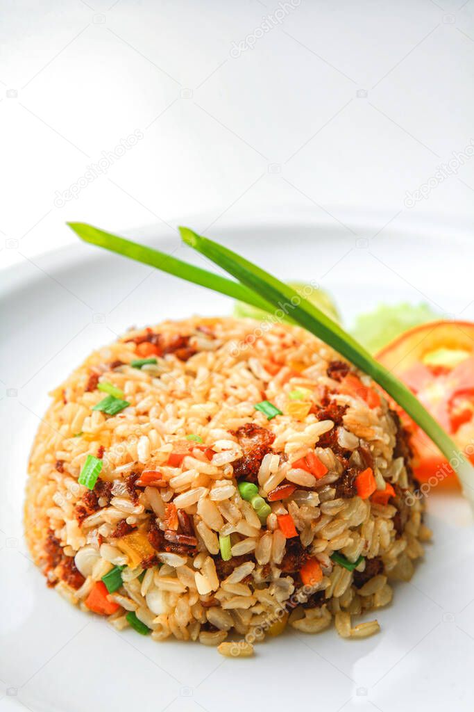 Asian fried rice with egg and vegetable in white ceramic plate on the table in the restaurant. Khao Pad popular Asian traditional style. Thai food. Front view with copy space.