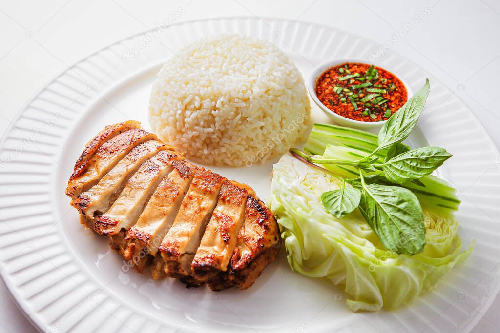 Grilled chicken rice with fresh vegetables in white ceramic plate on the table in the restaurant. Hainanese chicken rice popular traditional Thai style food. Healthy diet menu for lunch. Top view