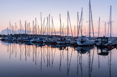 Limandaki yelkenli tekneler güzel günbatımında suya yansıyor.