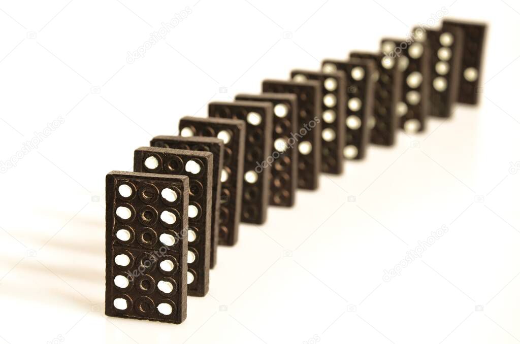 Black domino pieces standing in line in front of white background 
