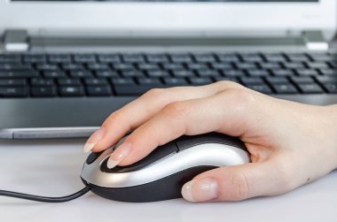 Dizüstü bilgisayarın önünde fare kullanan bir kadın.
