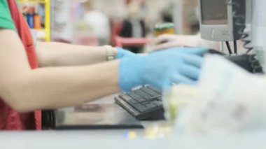 Süpermarketteki kasada çalışan bir işçi, emtia kasetindeki lastik eldivenli ürünleri kontrol ediyor. Coronavirus enfeksiyon koruması. Karantina için hazırlık.
