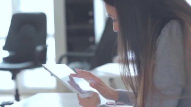 Ofisteki masada oturan ve ipad 'ini kullanan güzel bir kız. Orta boy. Yumuşak odak.