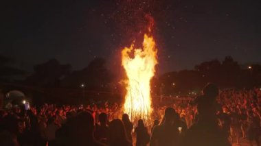 İnsanlar festivalde büyük bir şenlik ateşinin etrafında duruyorlar.