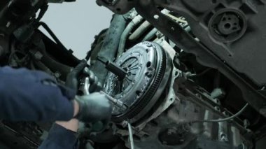 Auto mechanic in protective working gloves, unscrews the clutch pressure plate under the car engine