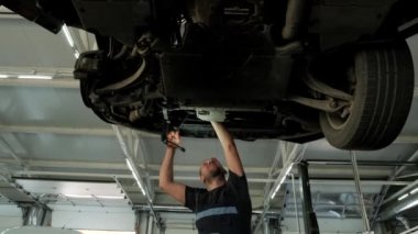 Otomobil tamircisi garajda araba kaldırma makinesinin altında çalışıyor. Otomobil tamirhanesi, araba servisi, tamirat..   