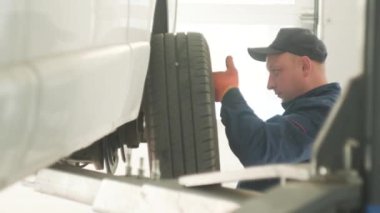 expert specialist technician changes tires, tyres of lifted up car, at auto workshop
