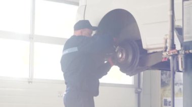Otomobil tamircisi oto tamirhanesinde kaldırılan otomobilin süspansiyonunu tamir ediyor.