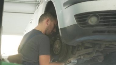 Tamir istasyonunda kaldırılan otomobilin tekerlek fren ayakkabılarını değiştiren araba tamircisi