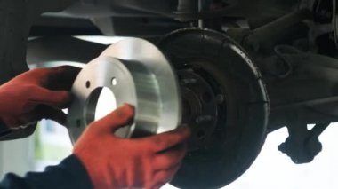 Tamir istasyonunda kaldırılan otomobilin tekerlek fren ayakkabılarını değiştiren araba tamircisi