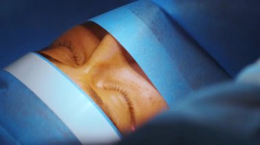 Lazer görüş düzeltmesi. Bir hasta ve bir cerrah ekibi göz ameliyatı sırasında ameliyathanede. Göz spekulumu. Lazer tedavisi. Hasta steril koruma altında.