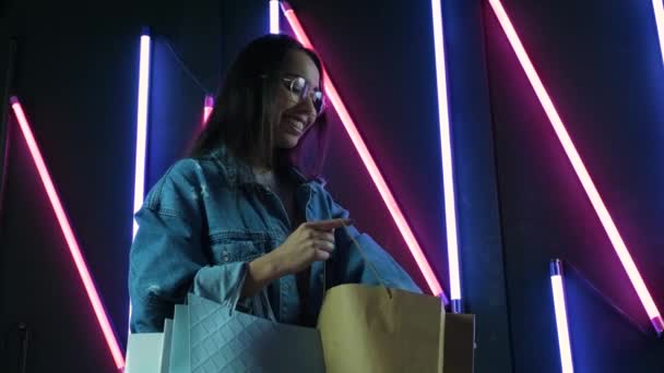 Jong Meisje Blauwe Denim Jas Met Boodschappentassen Neon Lampen Achtergrond — Stockvideo