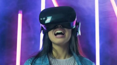Genç bir kadın şöyle bir etrafına bakıyor ve VR kulaklıkla ne kadar muhteşem olduğunu merak ediyor. Renkli duman arka planında sanal gerçeklik miğferi