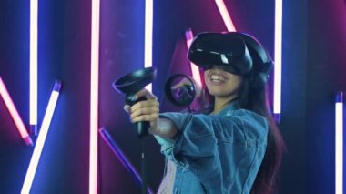 VR kulaklıkla oynayan ve gülümseyen genç bir kadın. Renkli ışıklandırma arka planında sanal gerçeklik miğferi