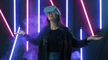 Genç bir kadın etrafına bakıyor ve VR kulaklıkla ne kadar harika olduğunu merak ediyor. Renkli duman arka planında sanal gerçeklik miğferi