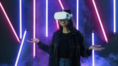 Genç bir kadın etrafına bakıyor ve VR kulaklıkla ne kadar harika olduğunu merak ediyor. Renkli duman arka planında sanal gerçeklik miğferi