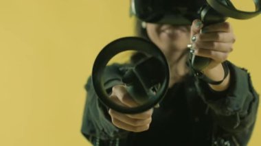 Genç bir kadın kumandayla oynuyor ve VR kulaklıkla ne kadar harika olduğunu merak ediyor. Sarı arka planda sanal gerçeklik miğferi. 