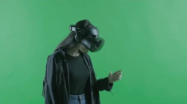 Genç bir kadın etrafına bakıyor ve VR kulaklıkla ne kadar harika olduğunu merak ediyor. Yeşil arka planda sanal gerçeklik kaskı. Krom Anahtar