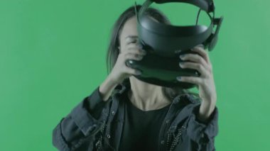 Genç bir kadın VR kulaklığı takıyor. Yeşil arka planda sanal gerçeklik kaskı. Krom Anahtar