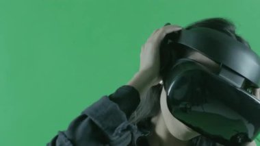 Genç, güzel, müzik dinleyen ve VR kulaklıkla dans eden. Yeşil arka planda sanal gerçeklik kaskı. Krom Anahtar