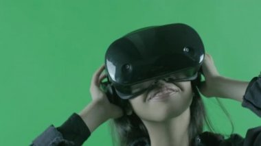 Genç kadın müzik dinliyor ve VR kulaklıkla dans ediyor. Yeşil arka planda sanal gerçeklik kaskı. Krom Anahtar