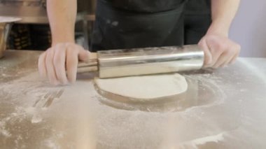 İtalyan pizza şefi un kaplı bir zeminde hamur yapıyor ve hamuru yuvarlıyor.