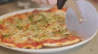 Pizza kesicisiyle pizzayı dilimleyen kişinin yavaş çekim yakın çekimi.