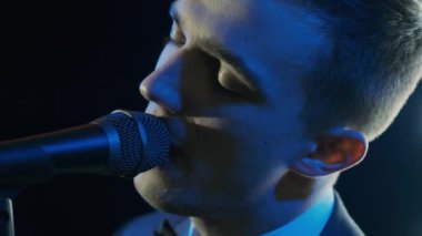Rock konserinde sahne performansı sırasında mikrofonla şarkı söyleyen bir adam. Erkek rock yıldızını kapat. Renkli ışık arka planında müzik konseri ver.