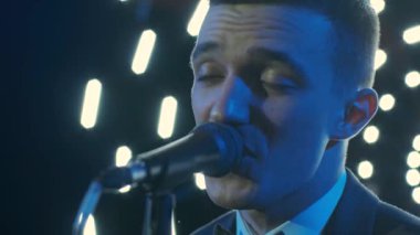 Rock konserinde sahne performansı sırasında mikrofonla şarkı söyleyen bir adam. Erkek rock yıldızını kapat. Renkli ışık arka planında müzik konseri ver.
