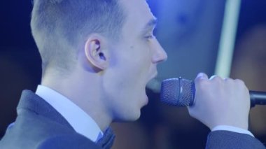 Rock konserinde sahne performansı sırasında mikrofonla şarkı söyleyen bir adam. Erkek rock yıldızını kapat. Renkli ışık arka planında müzik konseri ver.