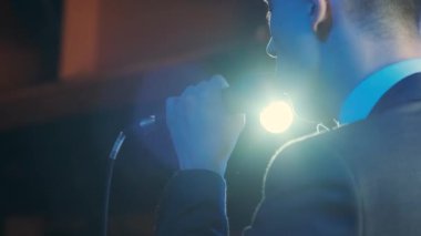 Rock konserinde sahne performansı sırasında mikrofonla şarkı söyleyen bir adam. Erkek rock yıldızını kapat. Renkli ışık arka planında müzik konseri ver.