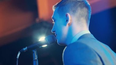 Rock konserinde sahne performansı sırasında mikrofonla şarkı söyleyen bir adam. Erkek rock yıldızını kapat. Renkli ışık arka planında müzik konseri ver.
