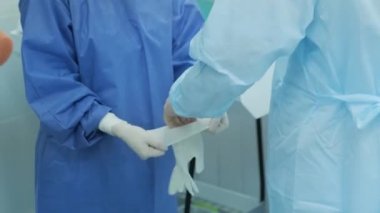 Ameliyattan önce cerrahın koruyucu eldivenleri takmasına yardım eden hemşire..