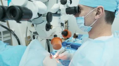 Cerrah ameliyathanedeki kadın hastanın gözündeki mikroskopu inceliyor. Göz ameliyatı sırasında mikroskop kullanan doktor katarakt ve diyopter düzeltmesi yapıyor..
