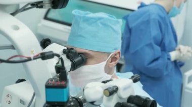 Cerrah ameliyathanedeki kadın hastanın gözündeki mikroskopu inceliyor. Göz ameliyatı sırasında mikroskop kullanan doktor katarakt ve diyopter düzeltmesi yapıyor..