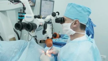 Cerrah ameliyathanedeki kadın hastanın gözündeki mikroskopu inceliyor. Göz ameliyatı sırasında mikroskop kullanan doktor katarakt ve diyopter düzeltmesi yapıyor..