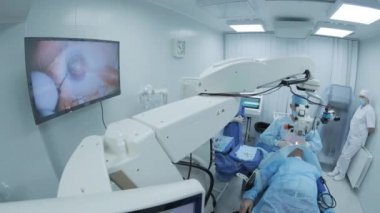 Cerrah ameliyathanedeki kadın hastanın gözündeki mikroskopu inceliyor. Göz ameliyatı sırasında mikroskop kullanan doktor katarakt ve diyopter düzeltmesi yapıyor..