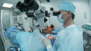 Cerrah ameliyathanedeki kadın hastanın gözündeki mikroskopu inceliyor. Göz ameliyatı sırasında mikroskop kullanan doktor katarakt ve diyopter düzeltmesi yapıyor..