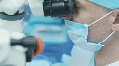 Cerrah ameliyathanedeki kadın hastanın gözündeki mikroskopu inceliyor. Göz ameliyatı sırasında mikroskop kullanan doktor katarakt ve diyopter düzeltmesi yapıyor..