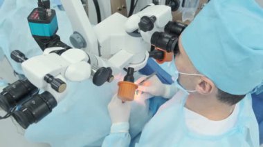 Cerrah ameliyathanedeki kadın hastanın gözündeki mikroskopu inceliyor. Göz ameliyatı sırasında mikroskop kullanan doktor katarakt ve diyopter düzeltmesi yapıyor..