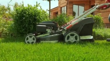 Çim biçme makinesi çimleri kesiyor. Bahçe işleri. Güneşli bahçede çim biçme makinesiyle çimleri biçmek. Bahçede çim biçme makinesiyle çalışan bahçıvan. Çim biçme makinesi yeşil çimleri kesiyor
