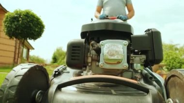 Çim biçme makinesi çimleri kesiyor. Bahçe işleri. Güneşli bahçede çim biçme makinesiyle çimleri biçmek. Bahçede çim biçme makinesiyle çalışan bahçıvan. Çim biçme makinesi yeşil çimleri kesiyor