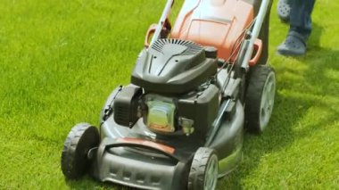 Çim biçme makinesi çimleri kesiyor. Bahçe işleri. Güneşli bahçede çim biçme makinesiyle çimleri biçmek. Bahçede çim biçme makinesiyle çalışan bahçıvan. Çim biçme makinesi yeşil çimleri kesiyor