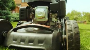 Çim biçme makinesi çimleri kesiyor. Bahçe işleri. Güneşli bahçede çim biçme makinesiyle çimleri biçmek. Bahçede çim biçme makinesiyle çalışan bahçıvan. Çim biçme makinesi yeşil çimleri kesiyor