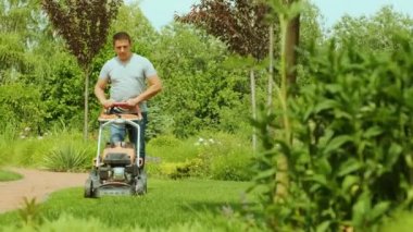 Çim biçme makinesi çimleri kesiyor. Bahçe işleri. Güneşli bahçede çim biçme makinesiyle çimleri biçmek. Bahçede çim biçme makinesiyle çalışan bahçıvan. Çim biçme makinesi yeşil çimleri kesiyor